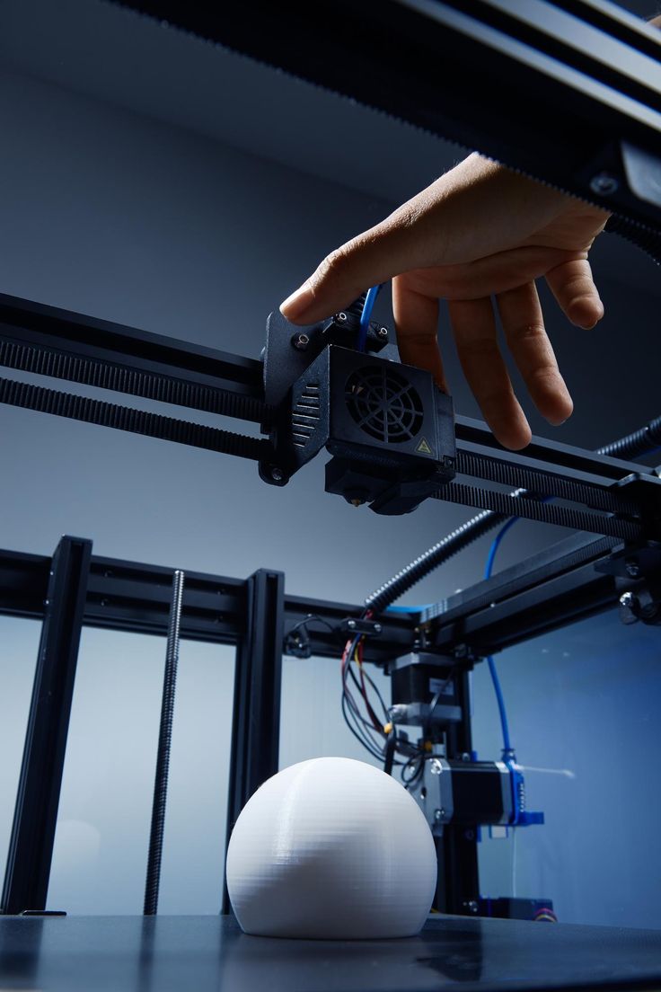 Close-up of a hand adjusting a 3D printer's extruder above a finished print